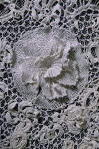 Daffodil made using Irish Crochet surrounded by other flowers on a lattice background.