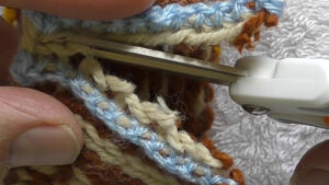 Scissors cutting a steek that has been reinforced using crochet