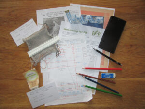 Pattern, swatch, pencils, measurement template, and other items used in adapting a pattern