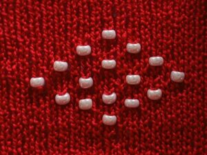 Diamond shape of white beads (machine) knit into a diamond on a background of red stocking stitch.