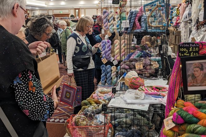 Photo of busy yarn show with customers admiring the offerings of colourful yarns on a stall.