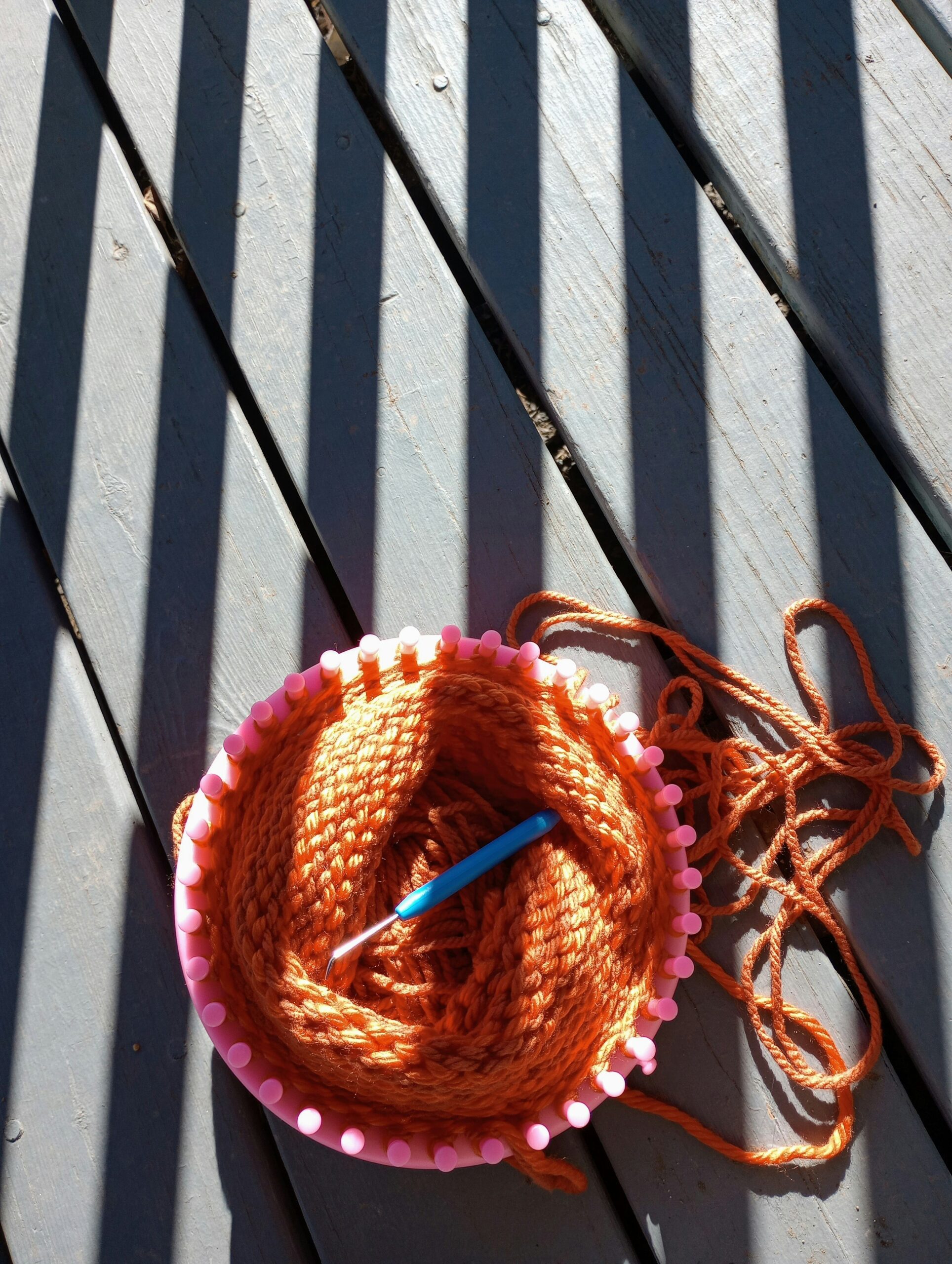 Loom knitting on wooden decking with shadows forming stripes